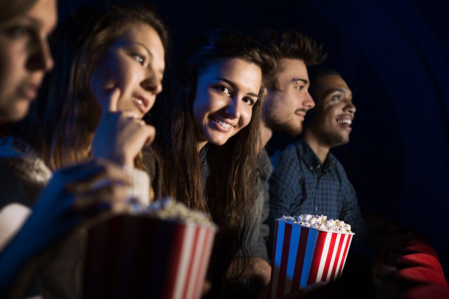 Group of teenager friends at the cinema watching a movie together and eating popcorn, entertainment and enjoyment concept